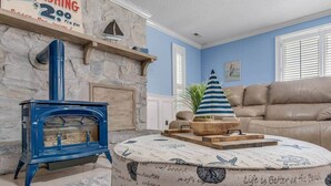 A living room with a blue wood-burning stove, a stone fireplace, a blue-striped umbrella, a beige sofa, and a nautical-themed ottoman.