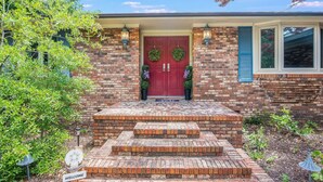 A brick house with a red door, two wreaths, and a welcome sign.