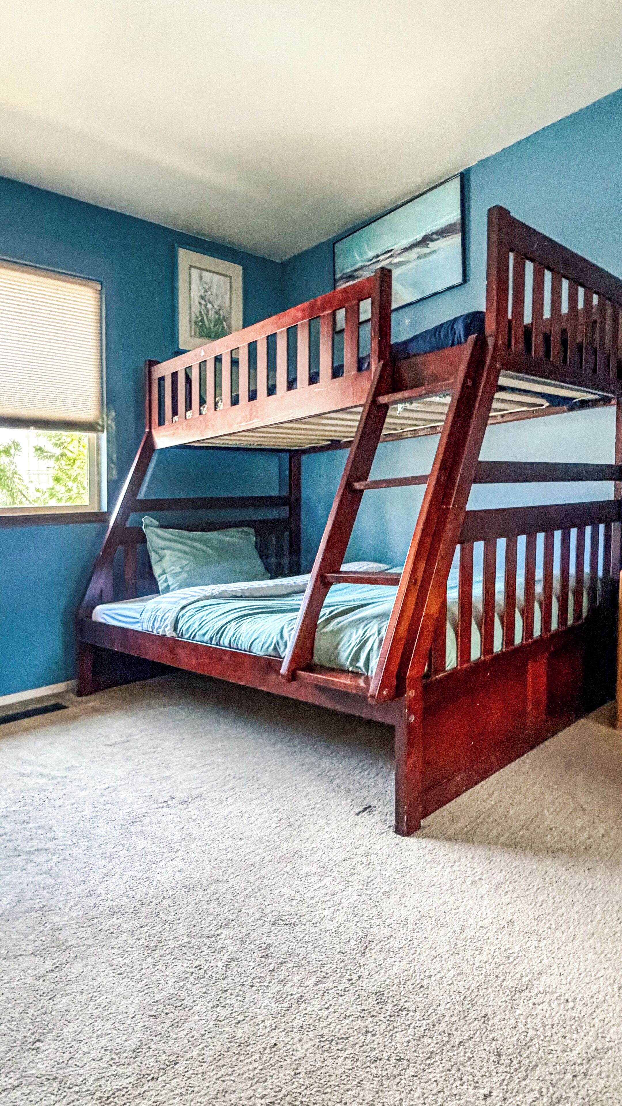 Een stapelbed in een kamer met blauwe muren, een raam en een vloerbedekking.