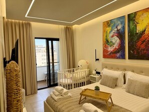 A modern hotel room with a bed, a crib, a small table, and a balcony with curtains.