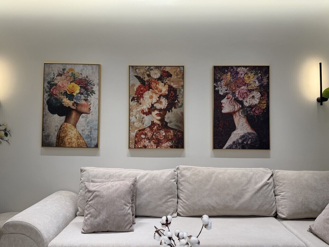 Une pièce comprenant un canapé, trois tableaux représentant des motifs floraux, encadrés, et un vase contenant des branches de coton.