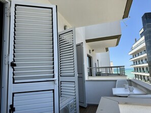 A balcony with a white table and chairs, a white door, and a view of the sea.