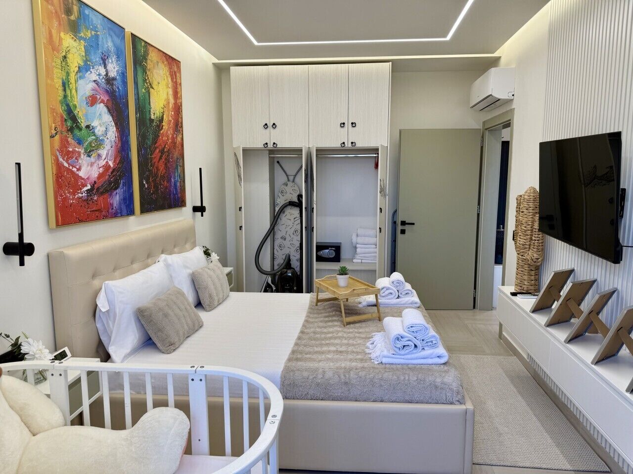 A modern bedroom with a bed, a crib, a TV, and a wardrobe.
