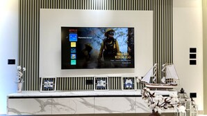 Ein modernes Wohnzimmer mit einem großen Flachbildfernseher an der Wand, einer Marmorarbeitsplatte und Dekorationsobjekten, darunter ein Schiffmodell und eine Vase mit Blumen.