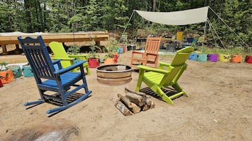 Un camping con dos sillas Adirondack, un brasero y un toldo.