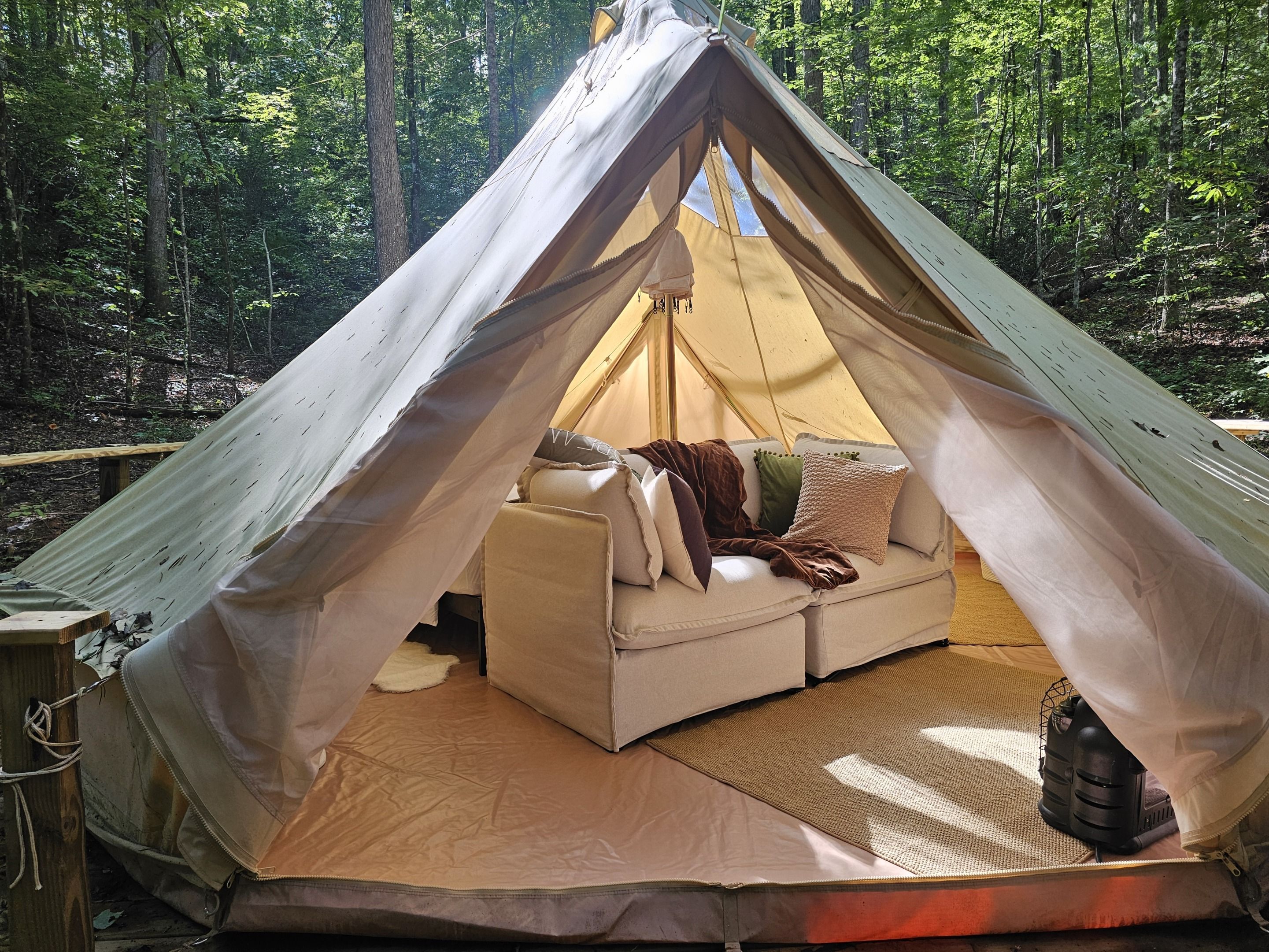 A tent with a cushioned seating area, a small table, and a lantern.