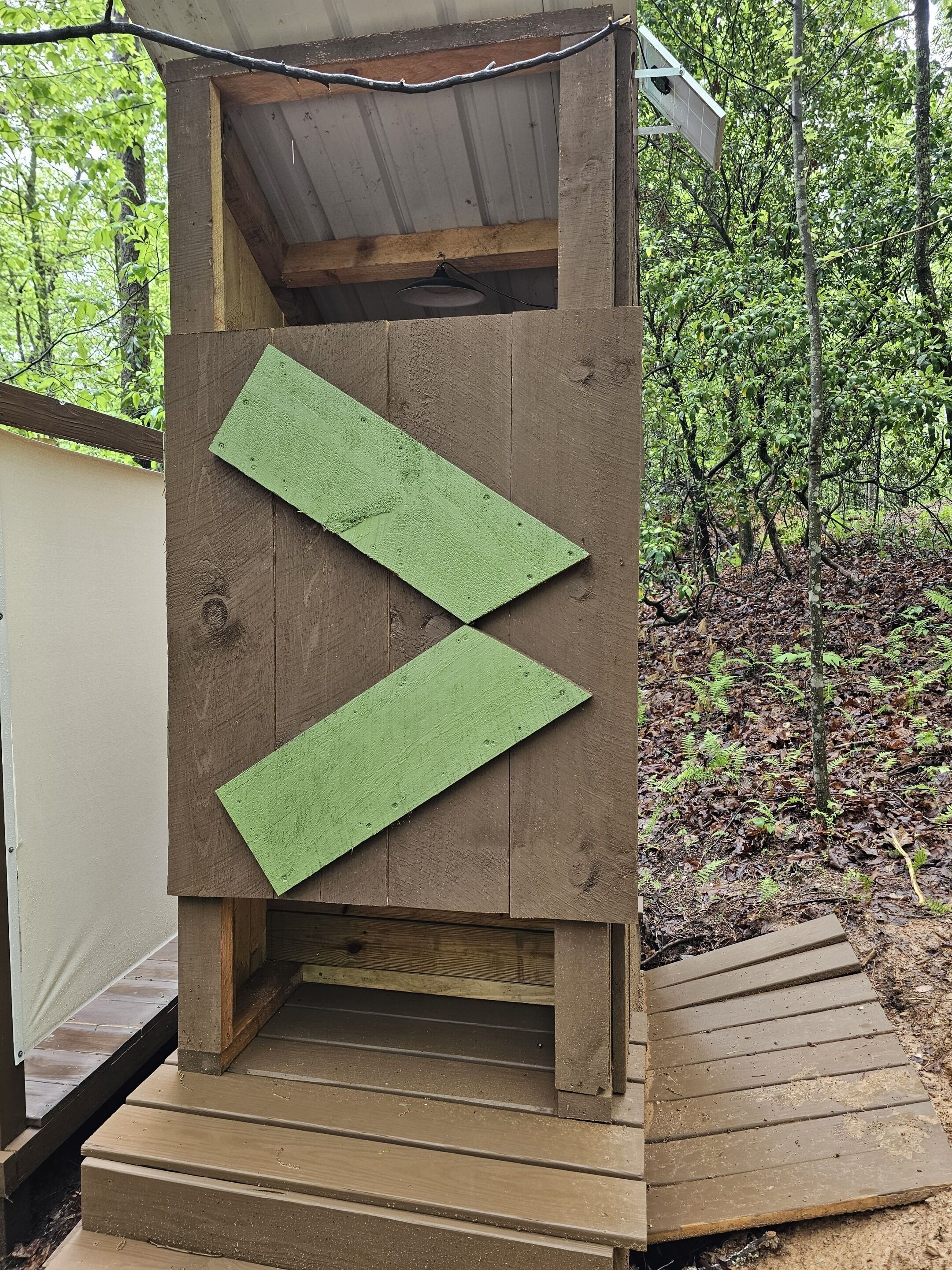A wooden structure with a green arrow design, a small porch, and a forested background.