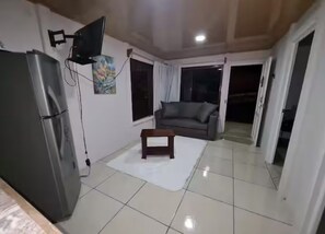 A living room with a flat-screen TV mounted on the wall, a small wooden table, a sofa, and a refrigerator. - Nice house with pool and terrace (El Castillo)
