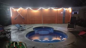 A swimming pool with a hot tub, surrounded by lounge chairs, and a covered area with lights.