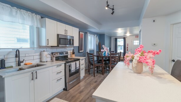 A modern kitchen with white cabinets, a microwave, an oven, and a dining area with a table and chairs.