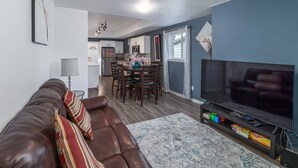 A living room with a brown leather sofa, a flat-screen TV, and a dining area with wooden furniture.