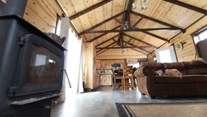 A rustic cabin interior with a wooden ceiling, a sofa, a television, and a kitchen area.