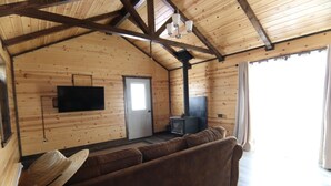 A wooden cabin interior with a sofa, a television, a door, and a fireplace.