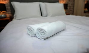 Cama bem arrumada com duas toalhas brancas dobradas sobre ela.