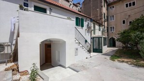 Une rue étroite bordée d’immeubles, avec une porte bien visible et un escalier menant à un étage supérieur.