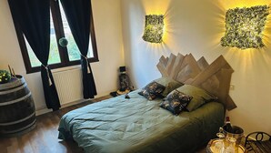 Ein Schlafzimmer mit einem Bett, einem Fenster mit Vorhängen, einem Heizkörper, einer Wandleuchte und einer Wanddekoration.