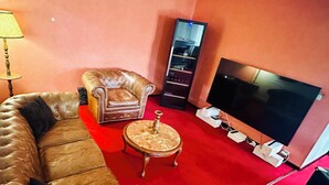 Ein Wohnzimmer mit braunem Ledersofa, einem passenden Sessel, einem kleinen Holztisch und einem an der Wand befestigten Flachbildfernseher.