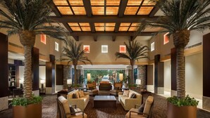 A spacious lobby with a central seating area, palm trees, and a view into a lush outdoor garden.