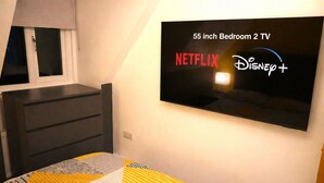 A bedroom with a 55-inch TV, a dresser, and a bed with a patterned bedspread. - Super Central 2 Bedroom Apartment Sleeps 5, 85` TV (Canterbury)