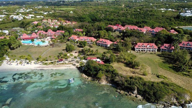 Oversigtsbillede af et resort med flere bygninger, en swimmingpool og en strand.