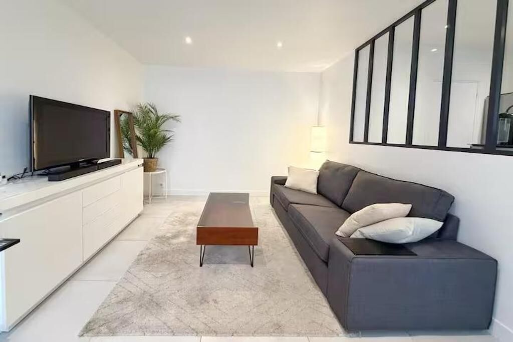 Un salon moderne avec un téléviseur à écran plat, un canapé, une table basse et une plante en pot.