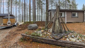 Una cabaña con terraza, rodeada de bosque y un pequeño estanque.