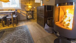 Una habitación acogedora con chimenea de leña, paredes de madera, una mesa de comedor con sillas y una alfombra estampada.