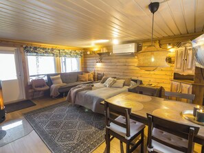 Ein gemütliches Blockhaus-Interieur mit Bett, Sofa, Esstisch und einer Pendelleuchte.