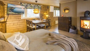Acogedor interior de cabaña con cama, una mesa de comedor, chimenea y vistas panorámicas.