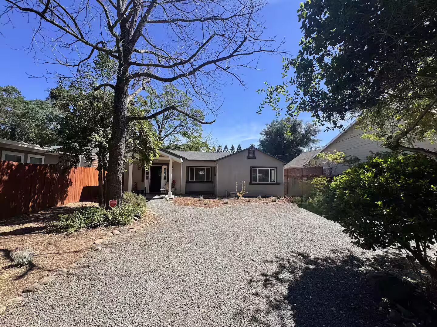 A residential property with a gravel driveway, a wooden fence, and a house with a front porch.