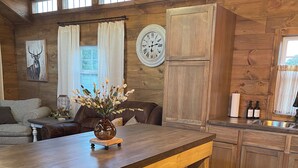 A rustic kitchen with wooden cabinets, a dining table, and a clock on the wall.