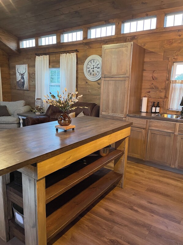 A rustic kitchen with wooden cabinets, a dining table, and a clock on the wall.