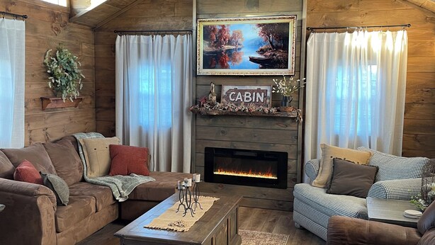 A cozy cabin interior with a fireplace, wooden furniture, and a large window.