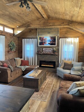 A cozy cabin interior with a fireplace, wooden furniture, and a large window.