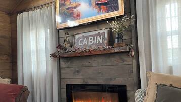 Una sala de estar con temática rústica, que incluye una chimenea, un televisor montado y un espacio de descanso acogedor.