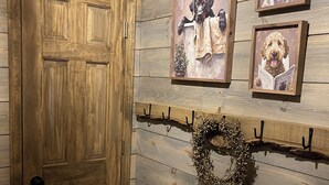 A wooden door, a wall-mounted wreath, and three framed dog paintings.