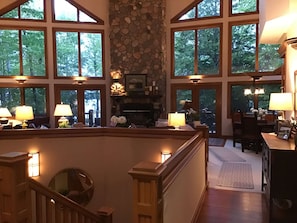 A spacious interior with large windows, a stone fireplace, and a wooden staircase. - After Dune Delight on Little Glen Lake (Empire)