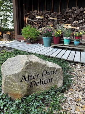 Een steen met de inscriptie 'After Dune Delight', omringd door groen en plantenpotten.