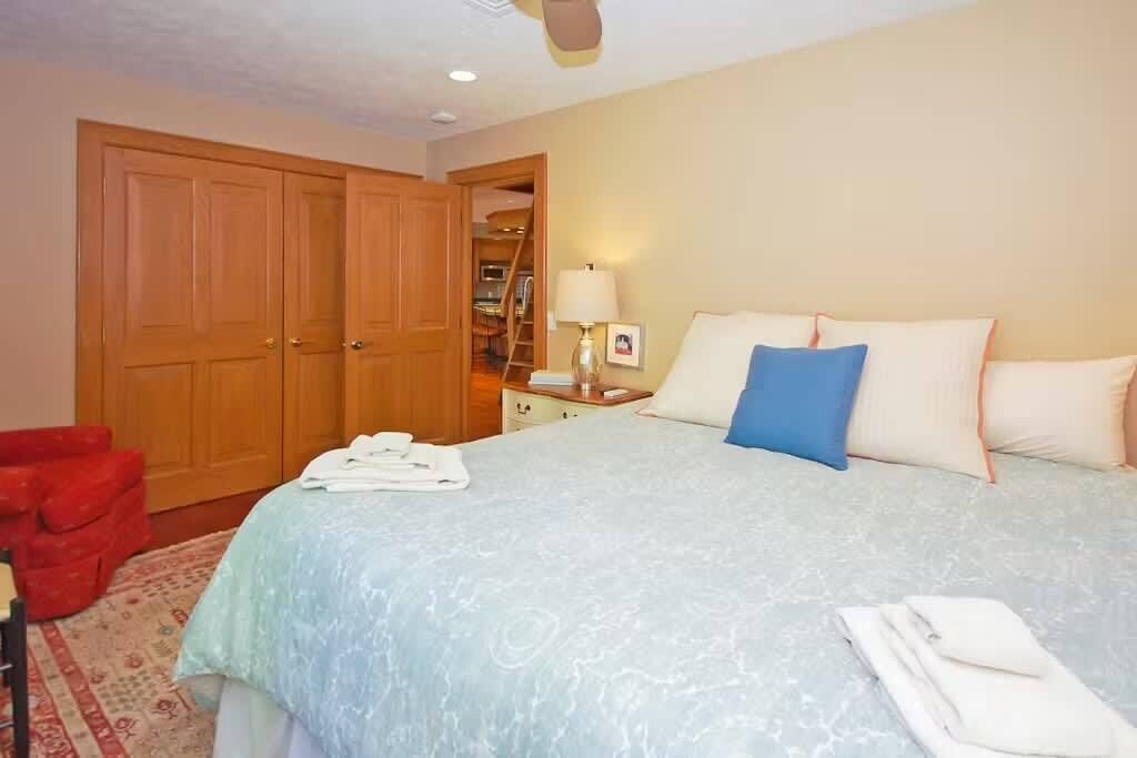 Une chambre à coucher avec un lit, une armoire, un bureau avec une lampe et une chaise rouge.