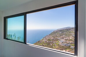 A window with a coastal view, including a town and the sea. - Hillside Villa • Private Heated Pool • Sunset Views • BBQ • Sea Panorama (Arco da Calheta)