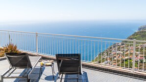 Un balcon avec deux chaises et une table, offrant une vue sur la côte et un ciel dégagé.