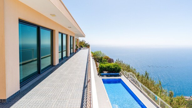 Un bâtiment moderne doté d’une piscine, de grandes fenêtres et offrant une vue sur la mer.