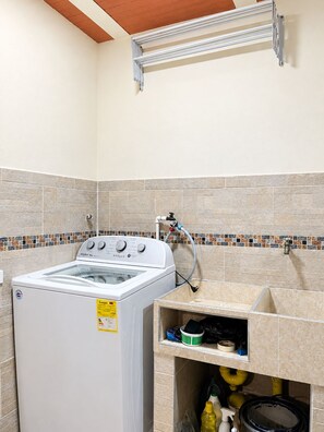 A laundry room with a front-loading washer and dryer, a tiled backsplash, and a shelf with cleaning supplies. - Wonderful 2-bedroom AC apartment in San Antonio - Cali (Cali)