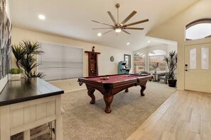 Une table de billard dans une pièce dotée d’un ventilateur de plafond, d’une armoire en bois et d’une porte dont les panneaux sont en verre dépoli.