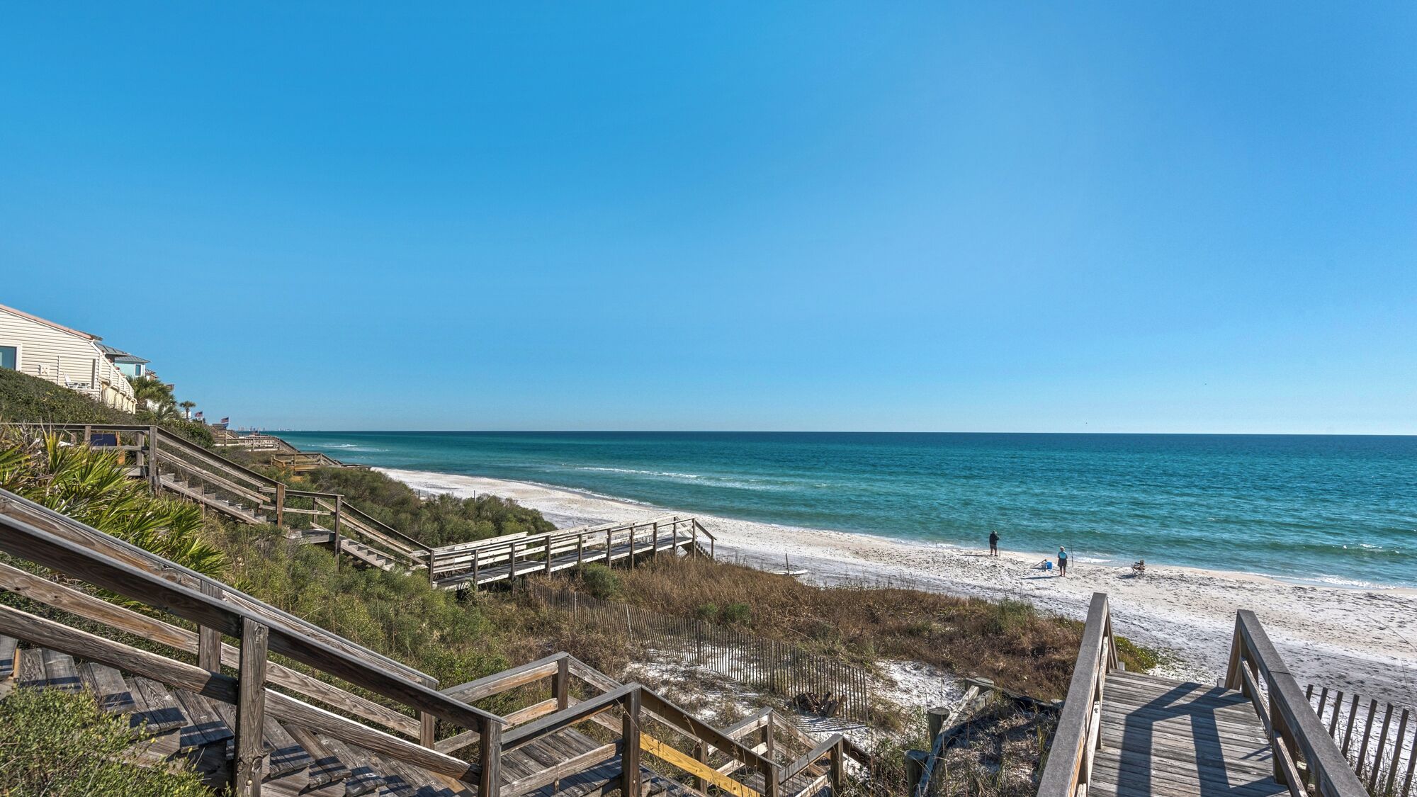 A beach with wooden boardwalks leading to the shore, clear blue sky, and calm ocean.
