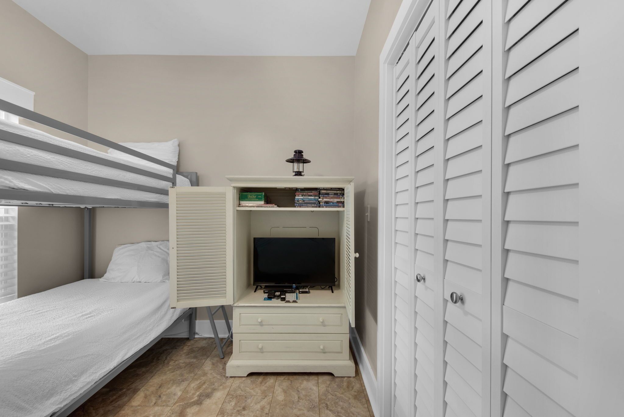 A bunk bed with a TV and storage unit, a closet with louvered doors, and a window with blinds.
