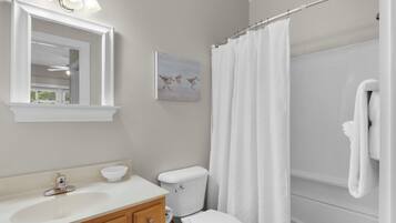 A bathroom with a sink, mirror, toilet, and shower curtain.