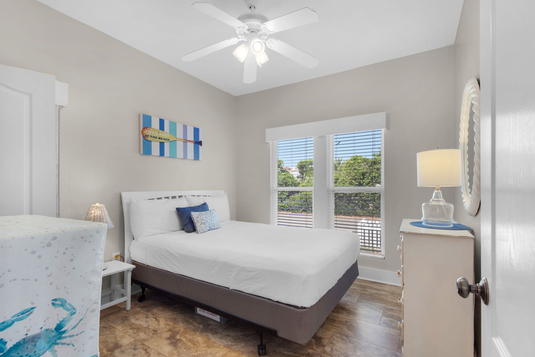 A bedroom with a bed, a ceiling fan, a window with blinds, and a nightstand.