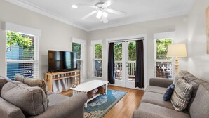 Uma sala de estar com ventilador de teto, televisão de tela plana, dois sofás, mesa de centro e porta de vidro deslizante que dá para uma área externa.