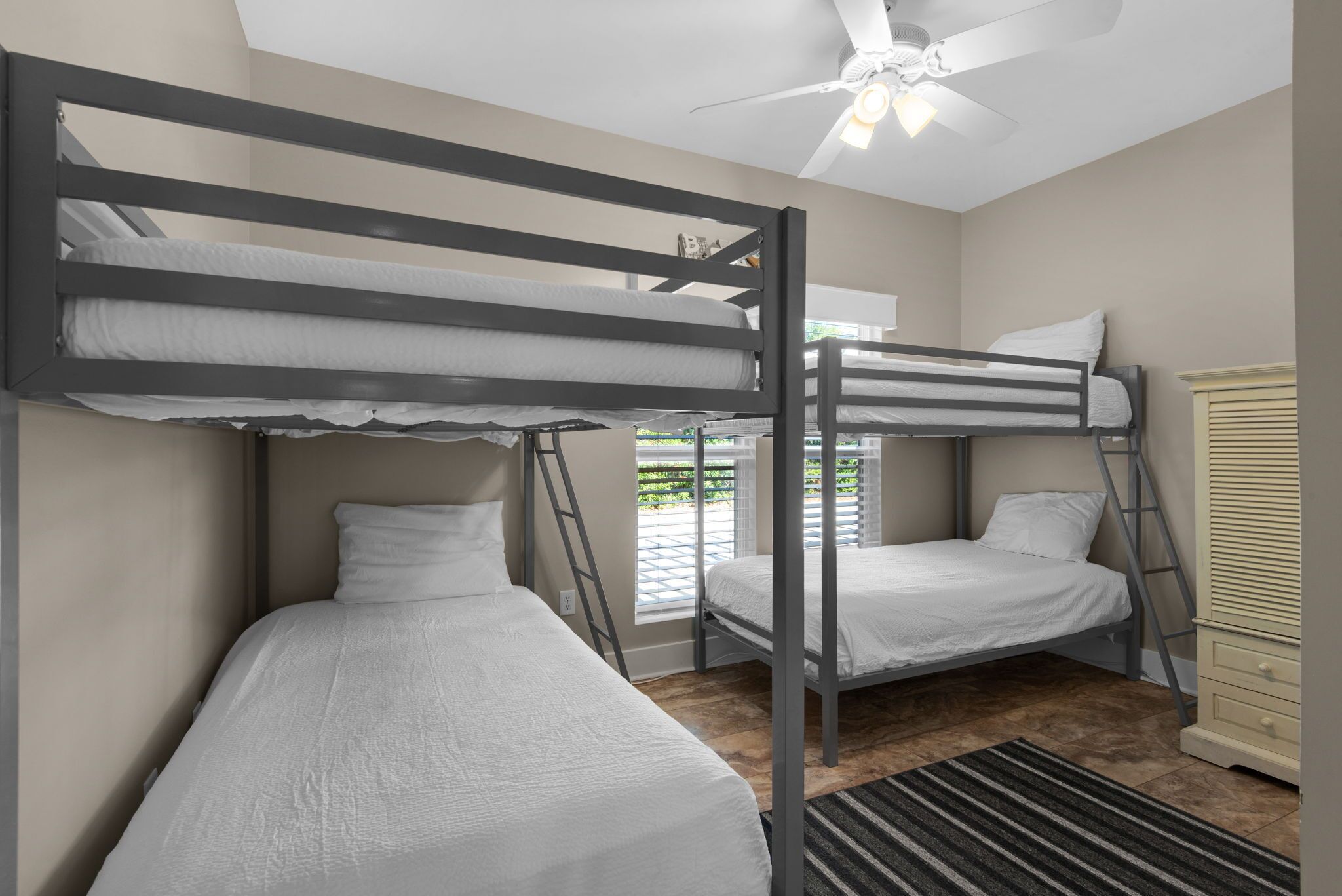 Ein Schlafzimmer mit Etagenbetten, einem Deckenventilator, einem Fenster mit Jalousien und Holzboden.